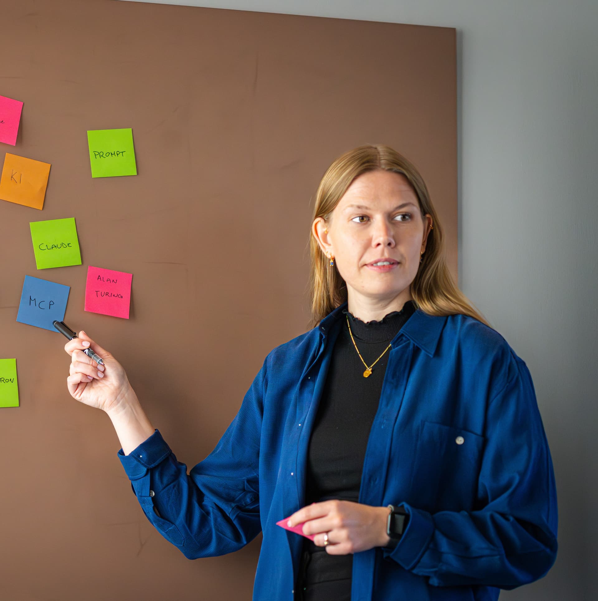 En kvinne presenterer og peker på post-it lapper organisert på en tavle under en workshop.En kvinne presenterer og peker på post-it lapper organisert på en tavle under en workshop.